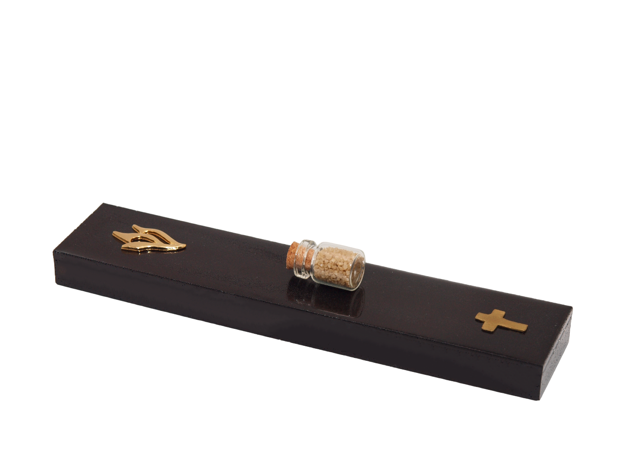 A black mezuzah case lying flat on white, with a gold shin at one end, a brass cross at the other and a small corked bottle of soil between them